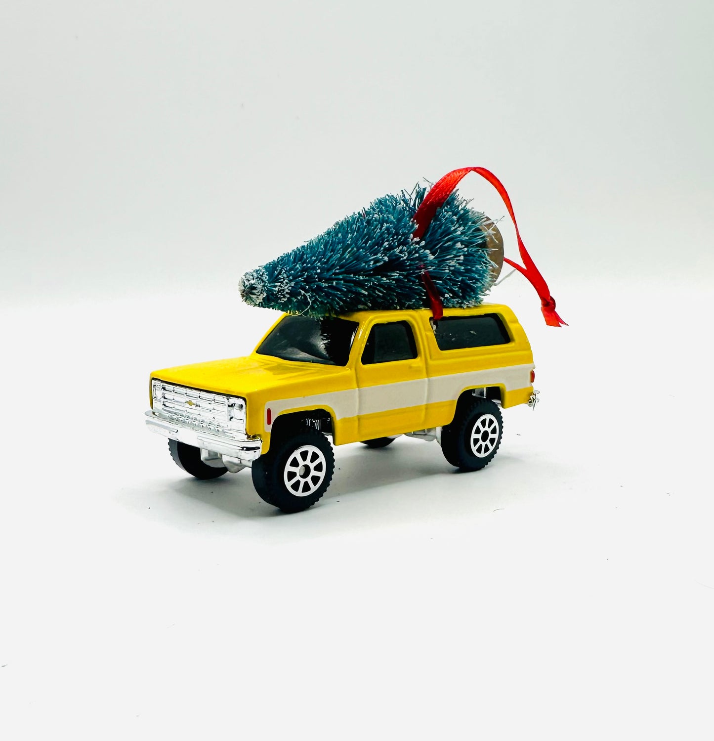 Yellow toy Chevrolet Blazer with a Christmas tree on top against a white background