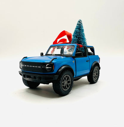 Blue toy Ford Bronco with a Christmas tree on a white background