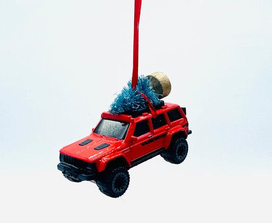 Red toy jeep with a Christmas tree on top, hanging from a red string against a white background.