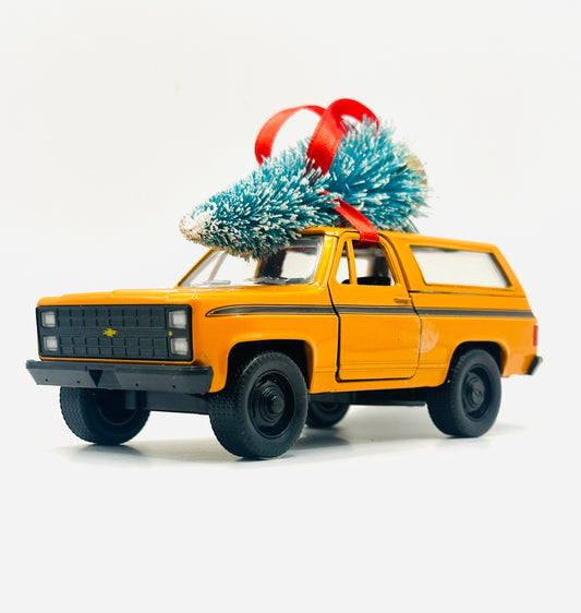 Orange Chevy Blazer K5 square-body diecast ornament with Christmas tree on roof and red ribbon - side view