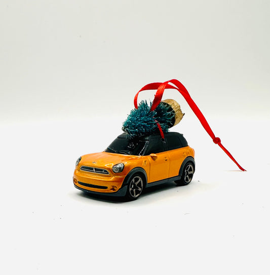 Model car with a Christmas tree on top, attached to a red ribbon against a white background